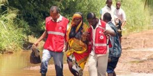 Four people wade through flood water on a sunny day