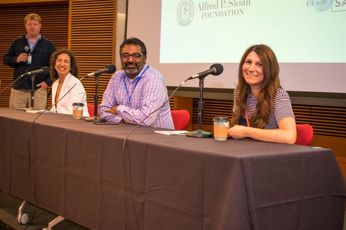 People at a table with microphones in front of a screen