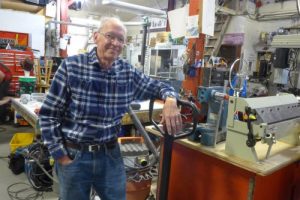 John Wiley standing in a workshop filled with machines, gadgets and tools